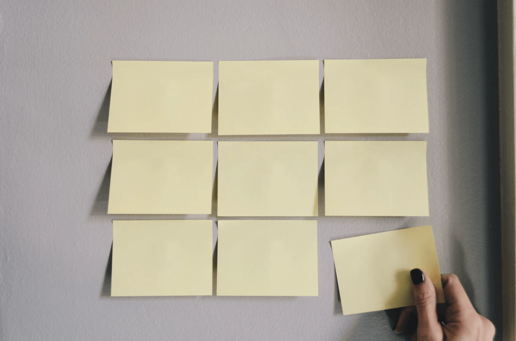 A wall with three rows of three sticky note each with someone placing the final sticky note. 