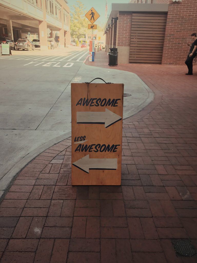 sign on street: aarow pointing to right with the heading "awesome", aarow pointing to the left with the heading "less awesome"